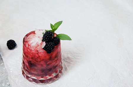 Ice cocktail with fresh mint and blackberries in a pink glass on a white background, white smooth tablecloth. Summer drinks.の写真素材