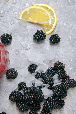 Closeup of blackberries with ice and slices of sappy lemon on a moist table with drops of water on a grey background.の写真素材
