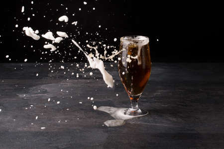 A big glass of beer full with brown ale and with white foam blowed away on a dark stone background. Alcohol beverage.の写真素材