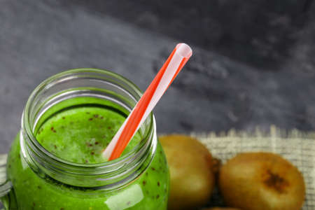 Close-up of a green cocktail. Kiwi smoothie and tropical fruits on a black background. Cold fruity drink with a straw.の写真素材