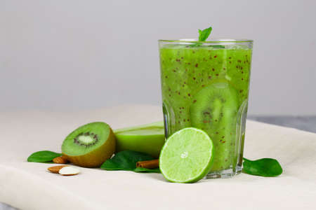 Close-up of a refreshing kiwi beverage on a beige table-cloth. A bright cocktail with fresh fruits on a gray background. Colorful kiwi, nuts, lime and apple half full of vitamins. Copy space.の写真素材