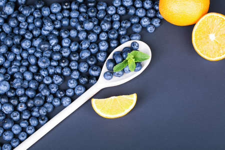 A composition of juicy blueberries, green mint, and ripe orange on a dark blue background. Fresh and organic berries and mint in a wooden spoon. Summer ingredients for a natural breakfast.の写真素材