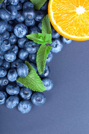 Close-up of fresh half of orange, healthy blueberries and green leaves of mint on a dark blue background. Copy space.の写真素材