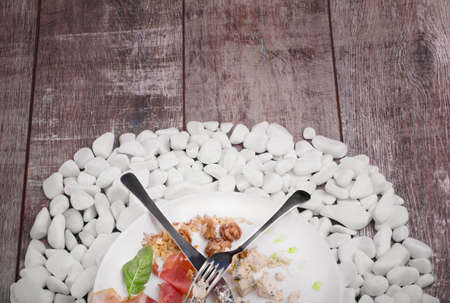 A plate with salted meat, cheese, walnuts and basil, a folk and a knife on a white stones and on a wooden background, top view.の写真素材