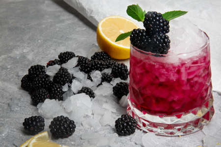 Ice coctail with mint and blackberries,in a pink glass on a grey background, berries, mint and a slice of lemon on a table-cloth.の写真素材