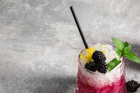 Summer ice fruit cocktail with blackberries, green leaves of mint, black drinking straw on a grey background, copy space.の写真素材
