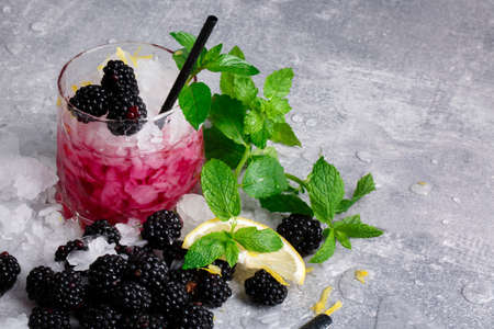 Cold drink with mint and blackberries in a huge glass on a grey background, slice of lemon with berries and mint on a table-cloth.の写真素材