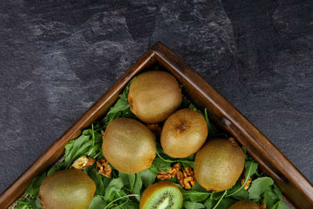 A wooden box with juicy kiwis in a mason jar on a dark gray background, top view. Kiwi on wooden tray. Copy space. Summer fruits.の写真素材