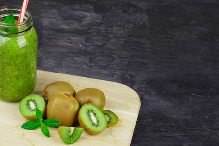 A mason jar filled with kiwi beverage, leaves of mint on a light wooden board on a dark stone background. Copy space.の写真素材