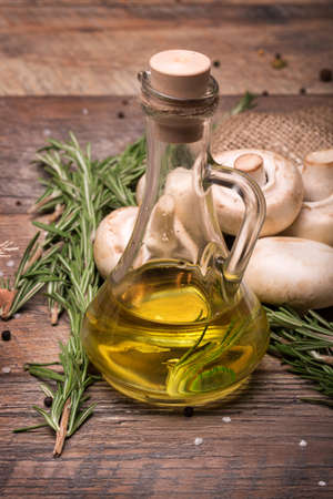 Close-up of a transparent jug full of sunflower oil on a brown wooden background. A few natural and organic mushrooms with branches of rosemary on the table.の写真素材