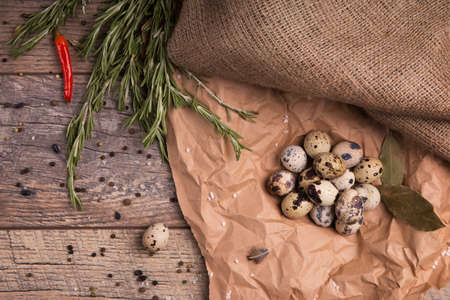 Top view of speckled quail eggs, bay leaves, grosery paper twigs of rosemary, red spicy chili pepper and different seasonings, healthy and refreshing diet on a light background.の写真素材