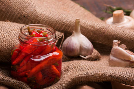 Closeup of a glass jar with chili pepper with spicy garlic, rustic table-cloth on a light wooden background.の写真素材