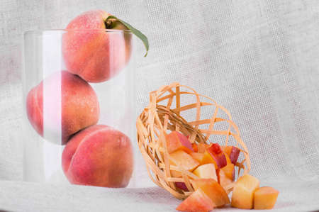 A composition of bright juicy peaches on a gray fabric background. A close-up of three whole peaches in a glass vase.の写真素材