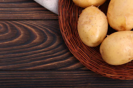 Closeup of new potatoes in a wooden plate, fresh tender vegetables for nutritious dishes on a dark brown background.の写真素材
