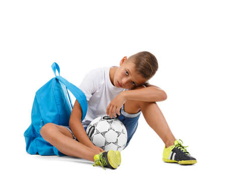 A cute boy with a bright satchel and a soccer ball isolated on a white background. A sitting child. Tired kid. Copy space.の写真素材