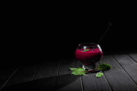 A wine-colored beet smoothie dessert. A big transparent glass filled with thick vegetable cocktail on a black background.の写真素材