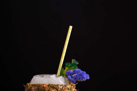 Macro picture of a pineapple cup full of juicy cocktail. A bright original drink on a black background. Summer ingredients.の写真素材