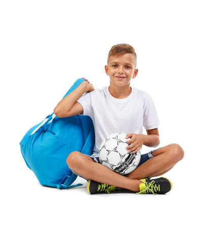 A happy schooler with a bright blue satchel sitting in a yoga pose. Cheerful child isolated on a white background. Sports concept.の写真素材