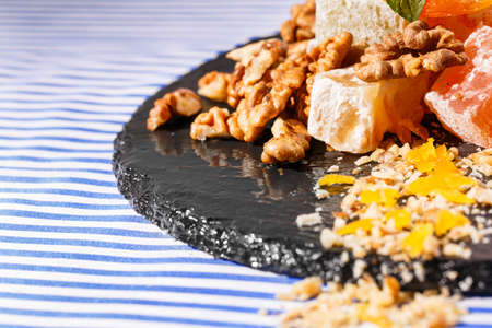 A beautiful composition of turkish delights, lokum or rahat lokum, walnuts and vivid green leaves of mint on a dark glass plate on a striped background, close-up. Sweets concept. Copy space.の写真素材