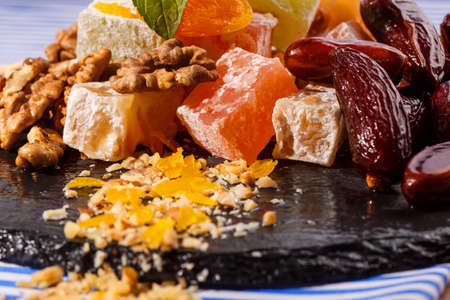 Sweets concept. Copy space. A plate with lokum, rahat lokum or turkish delight, brown date fruits, walnuts and mint on a striped tablecloth and on a dark plate, close-up.の写真素材