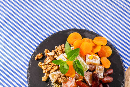 Closeup of turkish delight, lokum or rahat lokum, dry apricots, sweet date fruits, walnuts, bright aromatic leaves of mint on a striped background. Top view of sweets.の写真素材