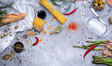 A top view of a great variety of pasta on a gray stone background. A bright set of ginger, olives, tableware, quail eggs, baguette, spices, asparagus, yellow bell pepper, red hot chili pepper.の写真素材