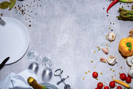 Bright yellow bell pepper, tomatoes, garlic and chili pepper on a gray stone background. A view from above on a beautiful composition. A plate with a cutlery next to different bright raw vegetables.の写真素材