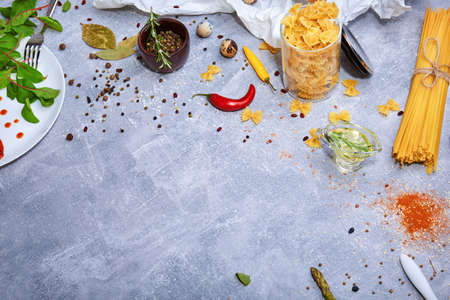 A view from above on a beautiful variety of pasta on a gray stone background. Different kinds of perfectly organized macaroni, a white plate, olive oil, red hot chili pepper, spices. Copy space.の写真素材