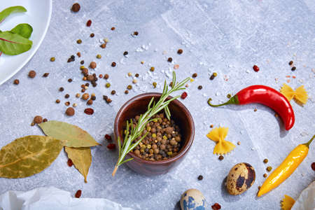 A view from above on fragrant ingredients. Seasoning on a gray stone background. A wooden bowl full of colorful spices next to bay leaves and bright chili peppers. Flavoring for taste. Copy space.の写真素材