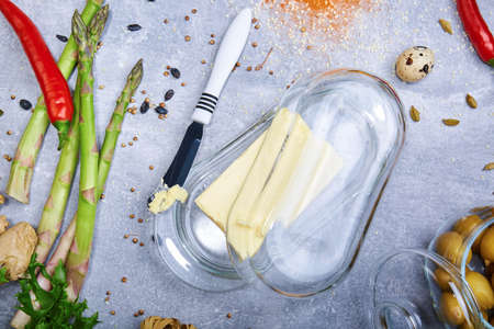Top view of a glass box of creamy, natural butter and a knife on a light table background. Fresh, healthful asparagus and hot red chili pepper. A quail egg and sour lemons. Lunch preparation concept.の写真素材