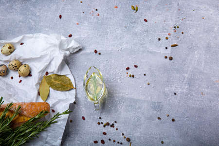 A view from above on food products on a grease-proof paper. Little quail eggs, baguette, dry bay leaves, rosemary twigs next to an oil tank. Food ingredients on a gray table background. Copy space.の写真素材