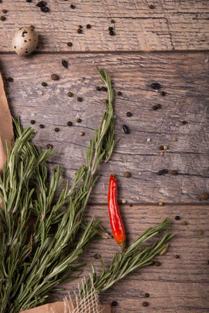 A single, whole chili pepper next to rosemary spices on a spacious wooden background. Natural greens and black pepper with a quail egg. Aromatic ingredients for a healthy mexican meal.の写真素材