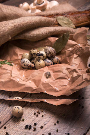 A pile of beautiful quail eggs on a crumpled paper on a wooden table background. Nutritious uncooked quail eggs. Protein ingredients for rustic homemade dishes. Boiled eggs with black pepper.の写真素材