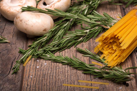 Macro picture of yellow uncooked noodles, mushrooms, and rosemary twigs. Uncooked ingredients on a wooden table background.の写真素材