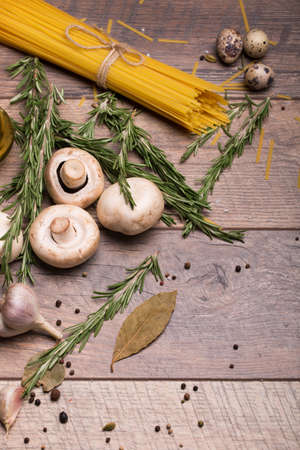 A view from above on a beautiful composition with pasta and eggs. Rosemary twigs, quail eggs, garlic, bay leaf, and mushrooms. A set of raw ingredients for dinner dishes on a wooden table background.の写真素材