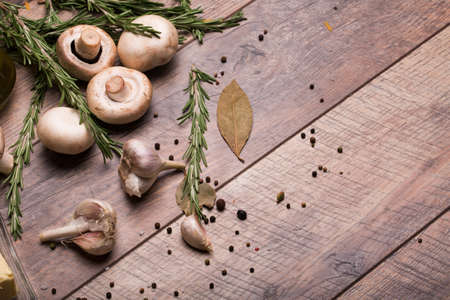 A close-up of mushrooms. Vegetable set on a wooden table background. Garlic, dry bay leaf and rosemary herbs. Copy space.の写真素材
