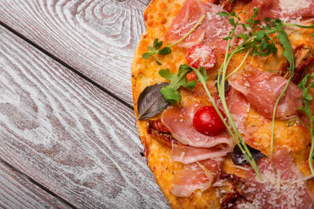 Top view of a pizza. Pizza with meat, cheese and vegetables on a wooden background. Italian cuisine concept. Copy space.の写真素材