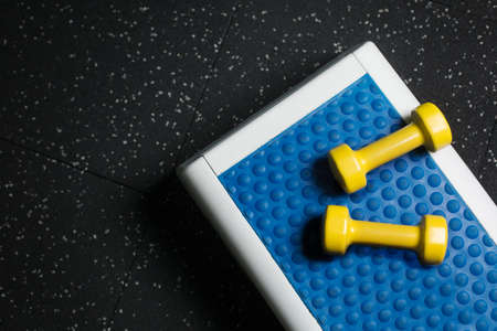Two bright yellow dumbbells on a blue step platform, stuff for sports competitions, gyms, training, workout, exercises for a healthy body on a dark blurred background.の写真素材