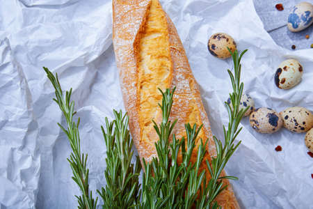 Closeup of wheat baguette, twigs of fragrant rosemary, little quail eggs on a light gray background.の写真素材