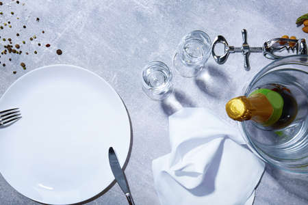 Closeup of white plate, fork, knife, green bottle of champagne, glasses, seasonings on a gray background.の写真素材