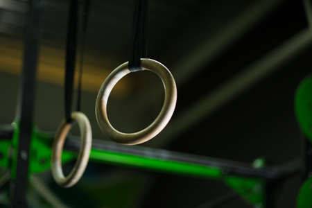 Closeup of two wooden still rings, steady rings hanging freely, supported by a strap on a dark blurred background.の写真素材