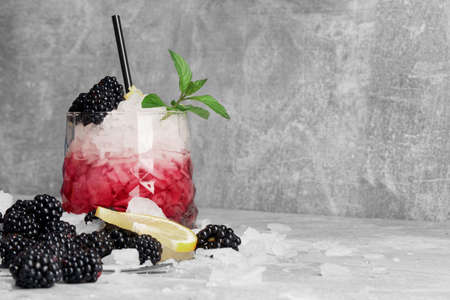 A huge glass of red fruit cocktail with ice, slices of fresh lemon, mint and blackberries on a light gray background.の写真素材