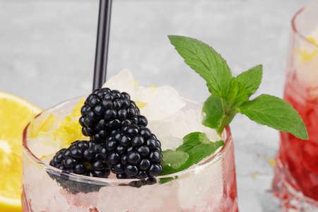 Closeup of a glass of fruit juice, succulent blackberries, green sappy leaves of mint on a light blurred background.の写真素材