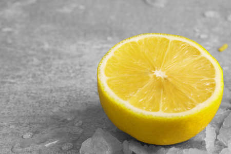 Closeup of a half of succulent yellow lemon, pieces of ice and drops of water on a light gray blurred background.の写真素材