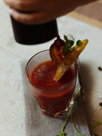 A top view of females hand sprinkles with pepper on a Bloody Ma