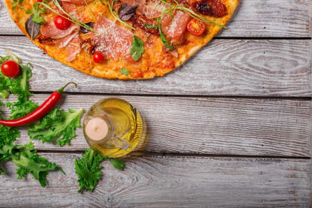 Italian pizza on a rustic table background, close-up. A half of meat pizza with salad leaves and olive oil. Copy space.の写真素材