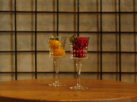 Two beautiful crystal wineglasses full of fruit ice cream. Colorful sorbet with decorative mint on a latticed background.の写真素材