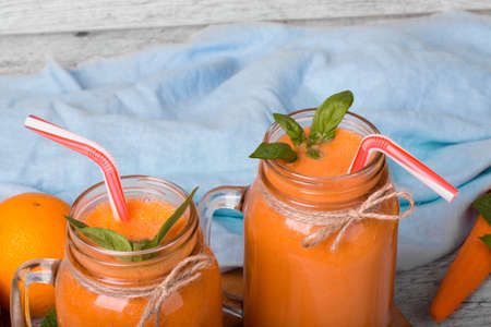 Close-up picture of an orange and carrot juice on a light blue decorative fabric background. Antioxidant juices for detox. A fruit cocktail with spicy mint and striped straws.の写真素材