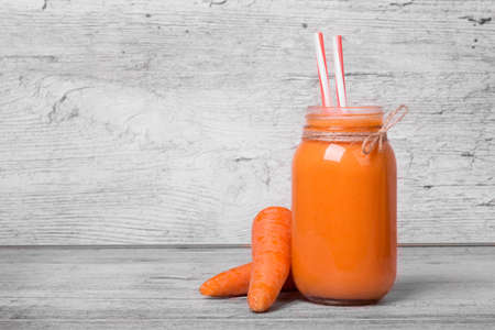 A glass of carrot milkshake or smoothie with drinking straw on a light wooden background, close-up. Bottle of fresh carrot juice with two whole carrots. Vegetable concept.の写真素材