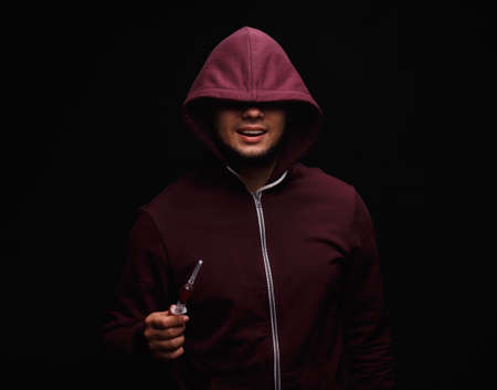 A young drug addict with a syringe on a black background. Portrait of young adult person with...